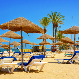 Strand-van-Sousse-met-palmbomen,-rieten-parasols-en-ligbedjes