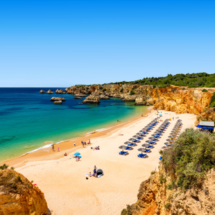 Breed zandstrand met ligbedjes tussen rotsen in mooie helderblauwe baai in de Algarve