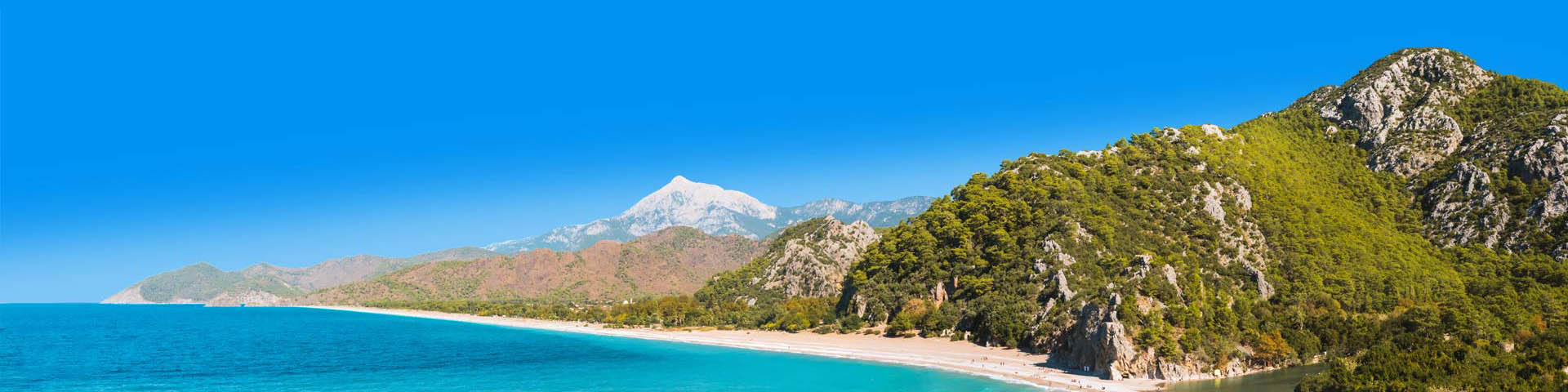 Kraakhelderblauwe zee met groene heuvelachtige rotsen aan de Lycische Kust van Turkije
