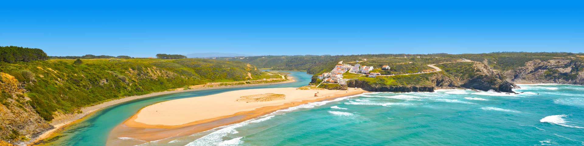 Strand met zee en rotsen met witte huisjes aan de kust van Portugal