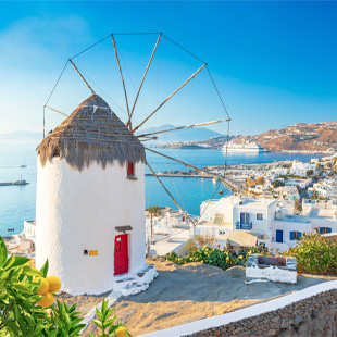 Traditionele witte windmolen in Mykonos met houten wieken, uitkijkend over zee en witgekalkte huizen langs de kust.