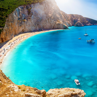 Turquoise baai van Porto Katsiki op Lefkas, met steile kalkstenen kliffen, licht zandstrand en enkele boten op helderblauw water.