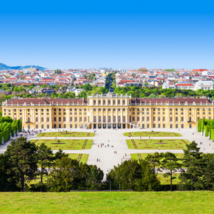 Uitzicht op Schloss Schönbrunn in Wenen met het lange gele paleis, symmetrische tuinen en bezoekers op het grote voorplein onder een blauwe lucht.