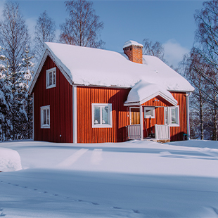 Rood houten chalet met wit dak in een besneeuwd landschap, omringd door kale bomen en een rustige winterse sfeer.