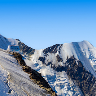 Steile, besneeuwde bergtoppen met ijs en rots, onder een heldere blauwe lucht, gezien vanaf een hoog bergpad.