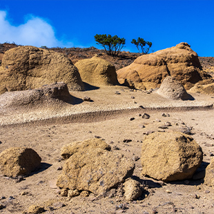 Droog maanlandschap in Teno Rural Park met grillige rotsen en zandpaden onder een heldere blauwe hemel.