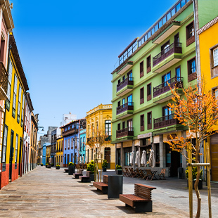 Gekleurde straat in La Laguna met pastelkleurige gevels, balkons en rustige wandelzone onder een blauwe lucht.