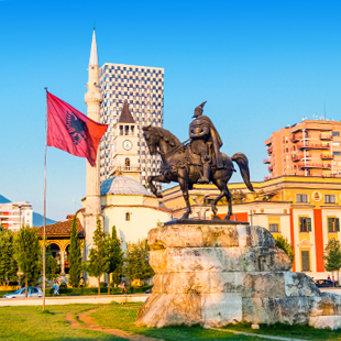 Standbeeld van een ruiter op een plein, met vlag, historische gebouwen en een minaret op de achtergrond.