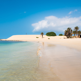 Breed zandstrand op Boa Vista in Kaapverdië met lichte duinen, turquoise oceaan en een uitgestrekte kust onder een heldere blauwe lucht.