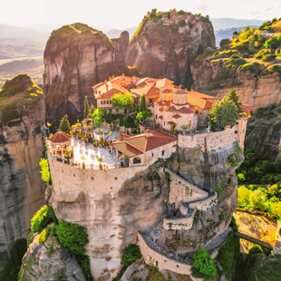 De zwevende kloosters van Meteora, gebouwd op hoge rotszuilen, omringd door groen en uitkijkend over het berglandschap.