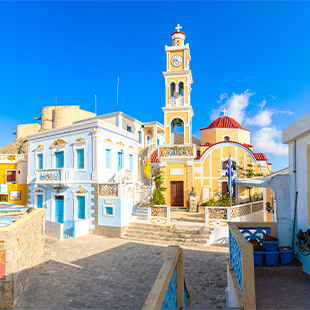 Kleurrijke straatjes op Karpathos met pastelgekleurde huizen, een kerk met klokkentoren en rode koepel, trappen en een helderblauwe lucht.