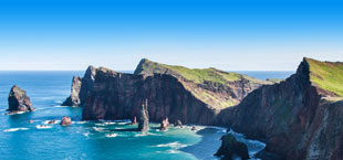 Rotsen rijzen op uit de oceaan bij de kust van Madeira, Portugal, onder een heldere blauwe hemel.