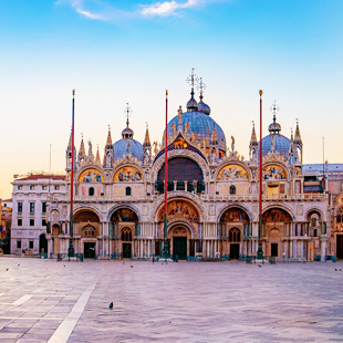 Gevel van de San Marco Basiliek met rijk versierde bogen en koepels, gezien vanaf het lege San Marcoplein onder een heldere lucht.
