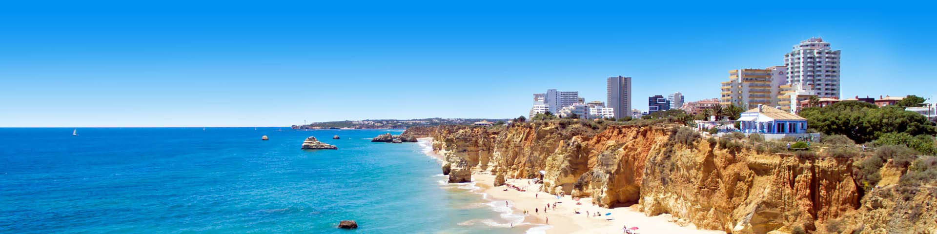 Prachtige Panorama van een Portugees strand met azuurblauwe zee, met bergen en stad in de verte. 