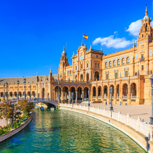 Het Plaza de España in Sevilla met halfrond gebouw, bruggen over een gracht en een ruim plein met sierlijke tegels onder een zonnige lucht.