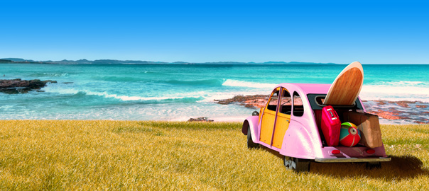Roze auto met surfplank en strandspullen aan zee