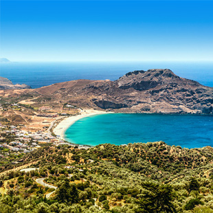 Uitzicht op de baai van Kreta met helderblauw water, rotsachtige kust en een klein eilandje voor de kust onder een zonnige, heldere hemel.
